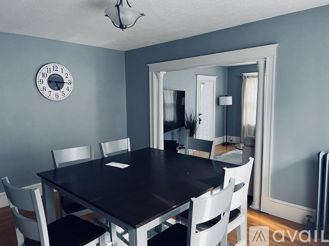 A dining room with a table and chairs and a clock on the wall.