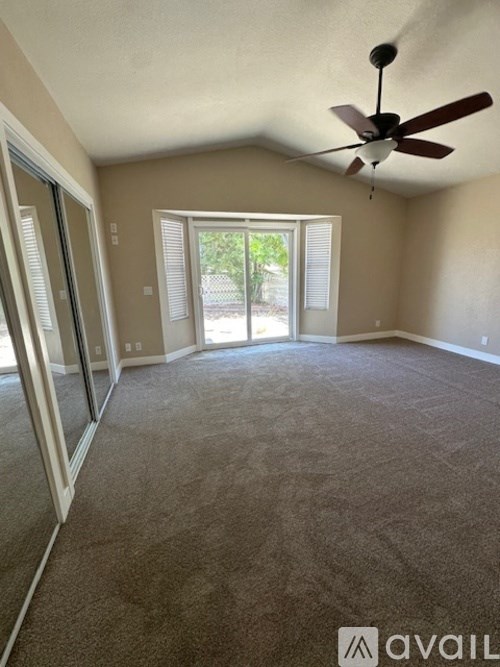 A room with a ceiling fan and sliding glass doors leading to a backyard.