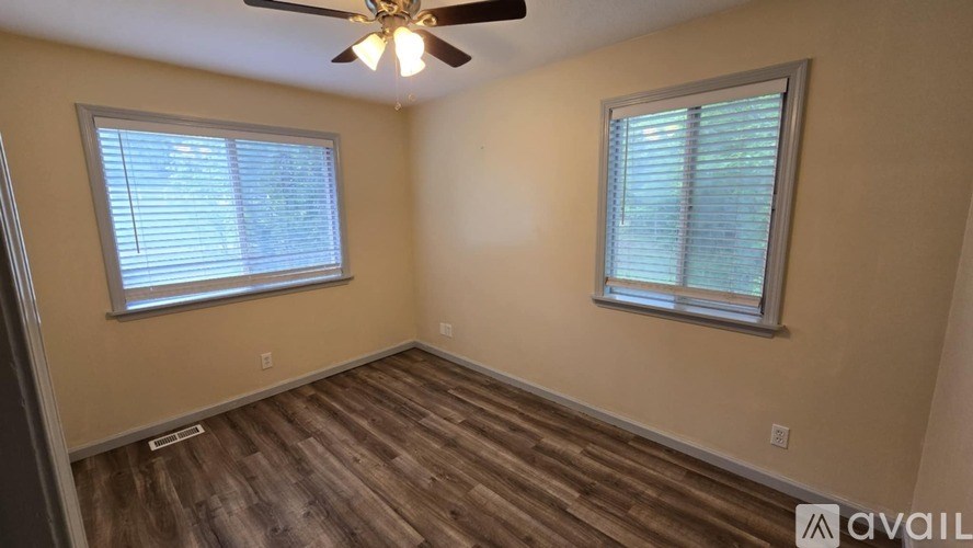 A room with a ceiling fan and two windows.