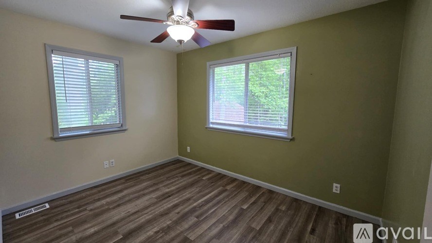 A room with a ceiling fan and two windows.