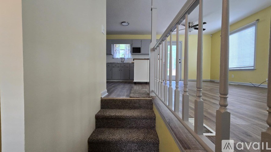 A staircase with a carpeted runner leads to a kitchen in the background.