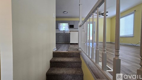 A staircase with a carpeted runner leads to a kitchen in the background.