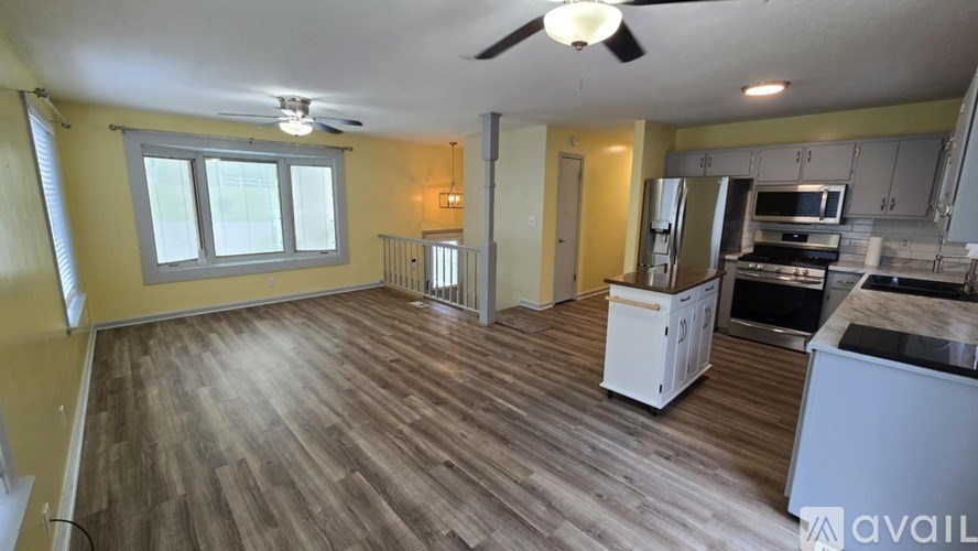 A spacious kitchen and living room with wooden floors and a ceiling fan.