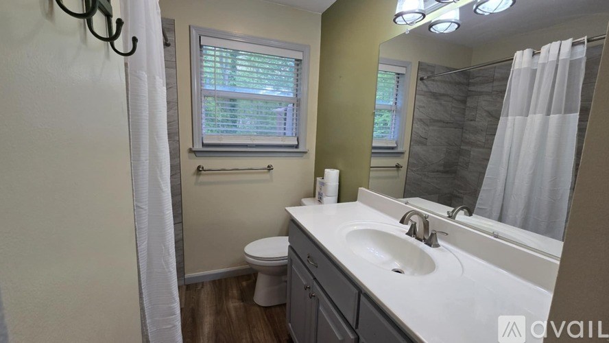A bathroom with a white sink, toilet, and a window with blinds.