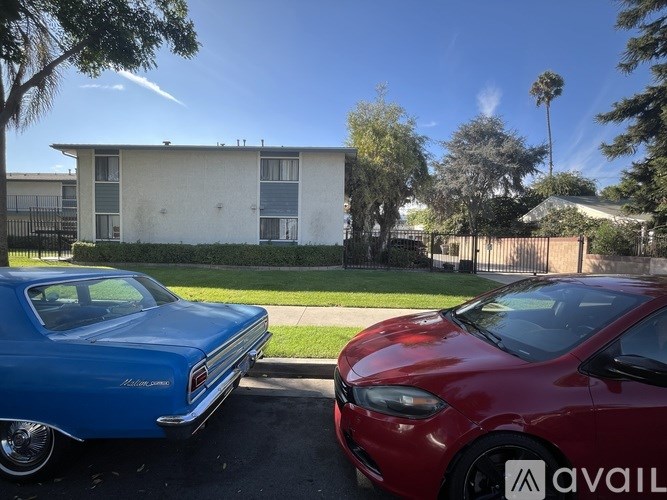 Two cars parked in front of a house with the word AVAIL on the side mirror of the red car.