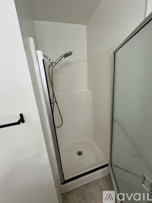 A shower area with a glass door and a black handle.