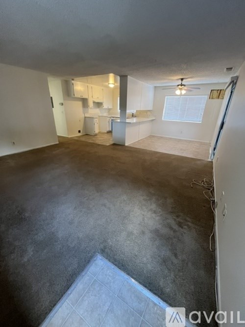 A spacious empty room with a kitchen area in the background.