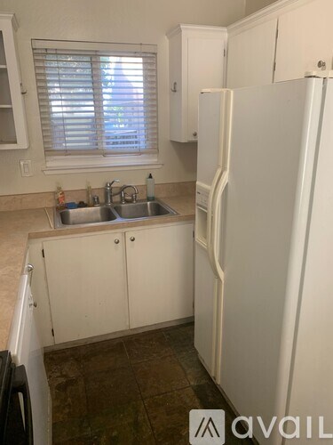 A kitchen with a sink, cabinets, and a refrigerator.