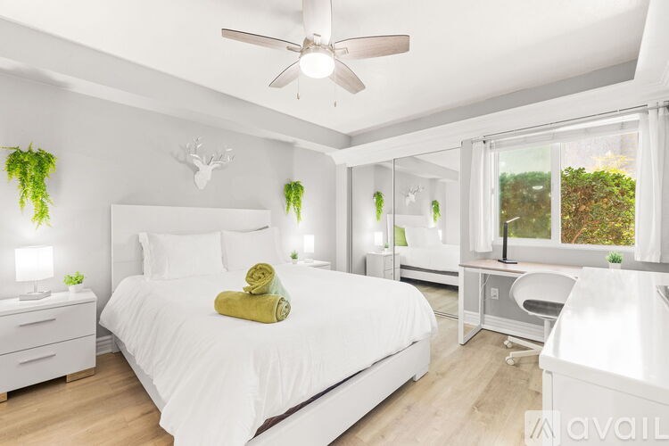 A bedroom with a large bed, a ceiling fan, and a window with a view of trees.