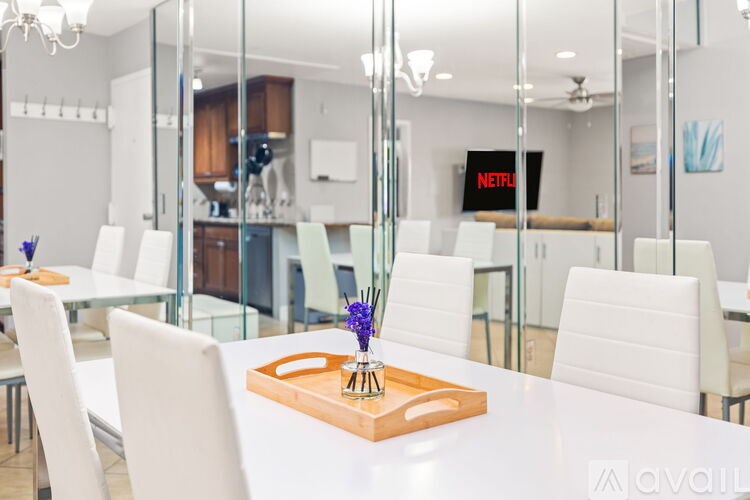 A white dining table with a wooden tray on it and a vase of flowers on top.