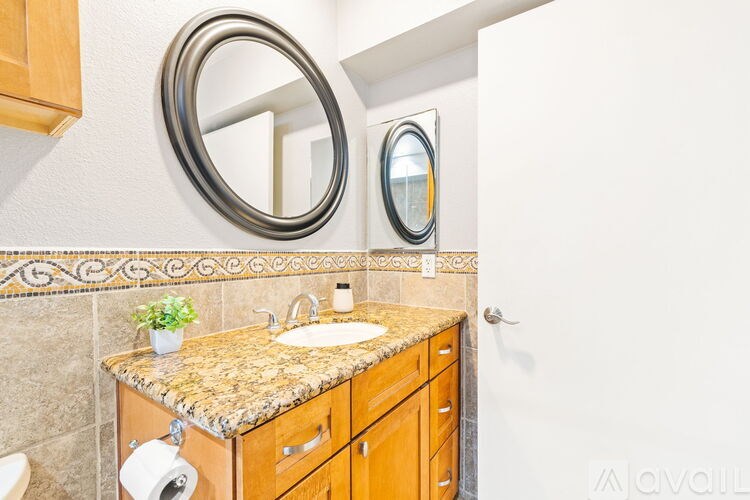 A bathroom with a granite countertop and a round mirror above it.