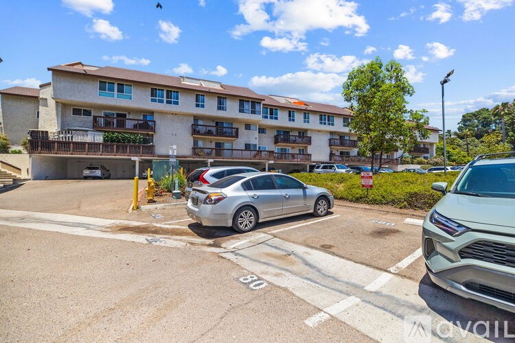 A silver car is parked in a parking lot in front of a multi-story apartment building.