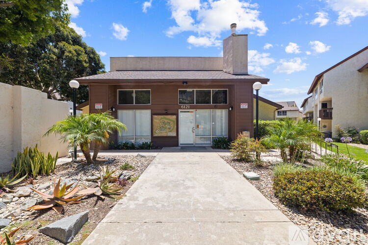 A house with a brown facade and a white door is surrounded by a garden.
