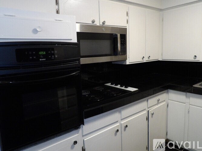 A black stove top oven sits next to a black microwave in a kitchen with white cabinets.
