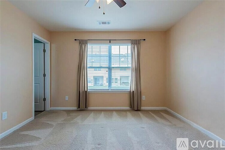 A room with a carpeted floor, a ceiling fan, and a window with blinds.