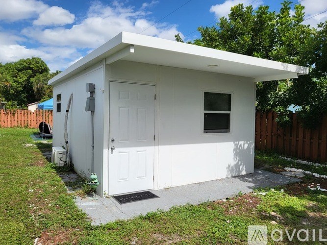 A small white shed with a door and a window is situated in a grassy area.