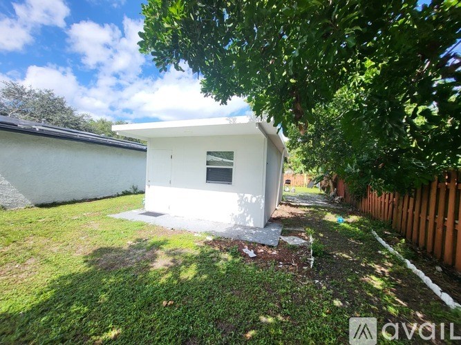 A small white house with a window is surrounded by greenery.