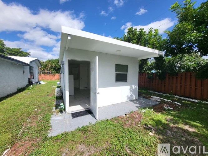 A small white house with a porch is surrounded by a grassy area and a wooden fence.