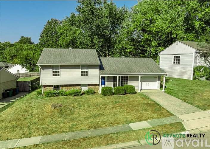A house with a green lawn and trees in the background is for sale.