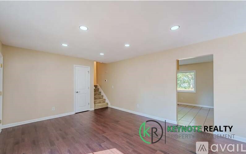 A spacious room with wooden flooring and a staircase leading to another room.