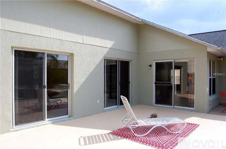 A patio with a chair and a red rug in front of a house.