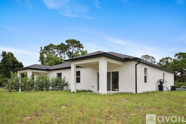 A white house with a black roof is surrounded by greenery and has a clear blue sky in the background.