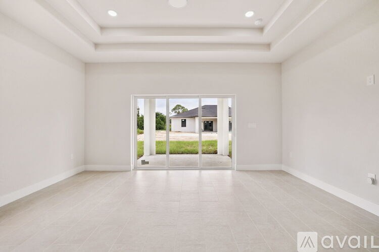 A spacious, empty room with a view of a house through a glass door.