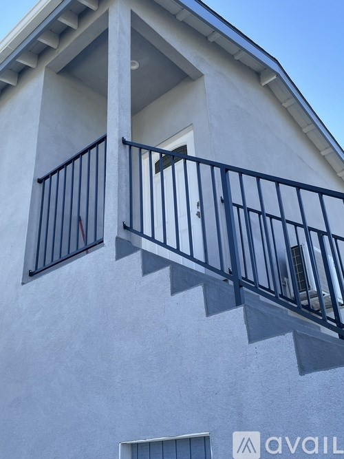 A white building with a black railing and a window with a sign that says "AVAIL".