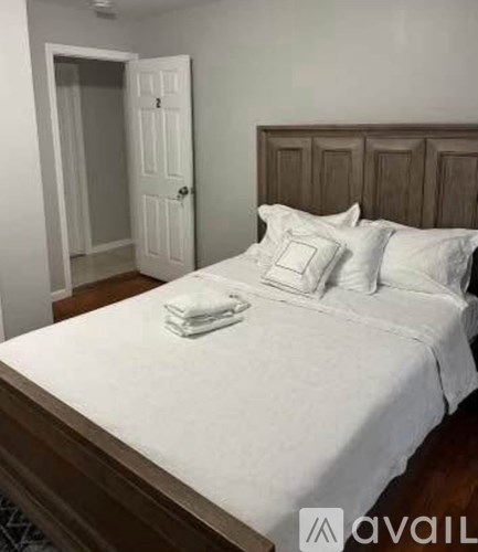 A bed with white bedding and two pillows is in the foreground with a white door in the background.