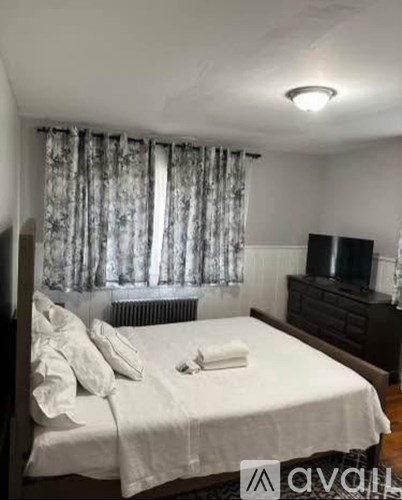 A bedroom with a bed, a dresser, and a window with curtains.
