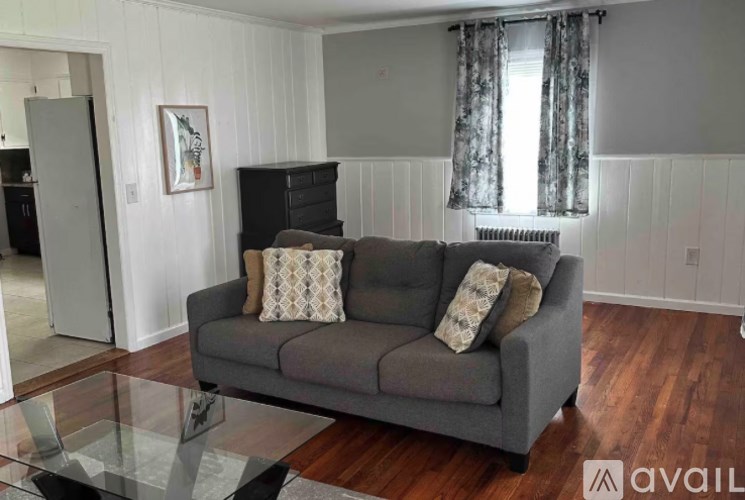 A grey couch with two pillows sits in a room with wooden floors and white walls.