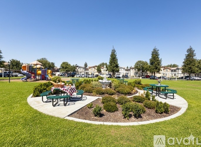A park with a picnic table surrounded by greenery and playground equipment in the background.