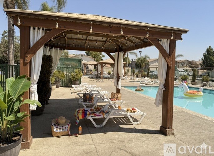 A wooden pergola with a table and chairs under it is set up next to a pool.