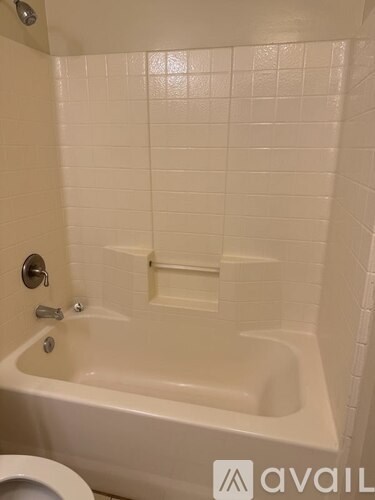 A white tiled bathroom with a bathtub and toilet.
