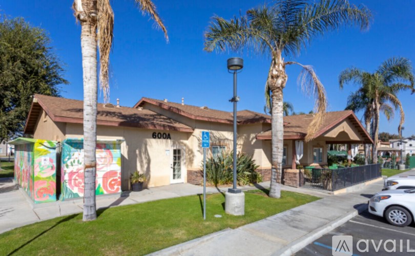 A street view with a building, palm trees, and a car parked on the side of the road.