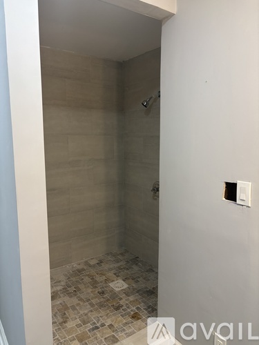 A tiled shower in a bathroom with a white wall and a light switch.