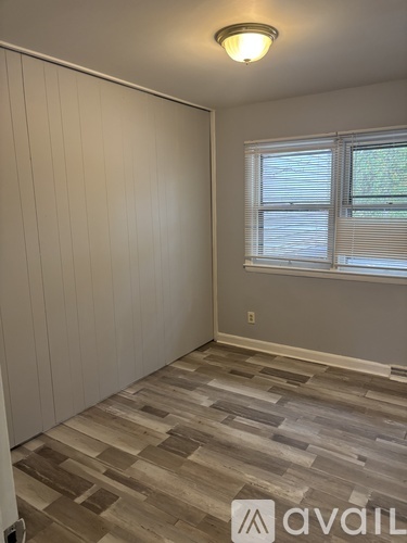 A room with wooden flooring and a window with blinds.