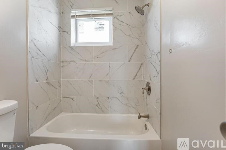 A white bathroom with a marble tile wall and a tub.