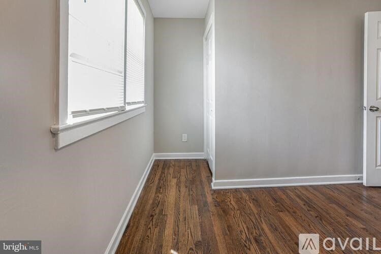 A room with wooden floors and white walls, with a window on the left and a door on the right.