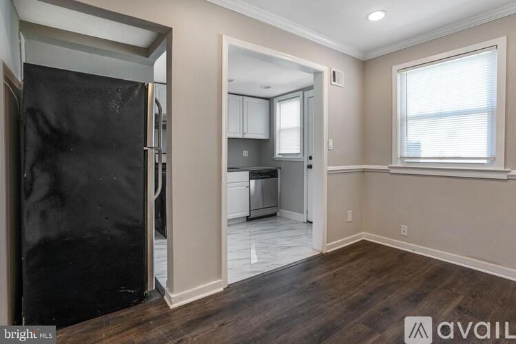 A kitchen with a black refrigerator is shown in a room with wooden floors and white walls.