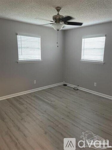 A room with a ceiling fan and two windows.