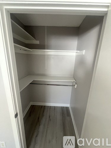 A small, empty, white closet with a wooden floor.
