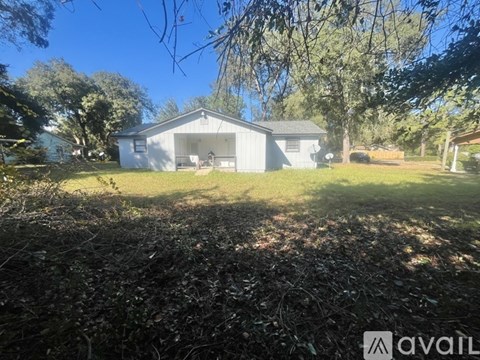 A house with a grey roof and white walls is surrounded by trees and grass.