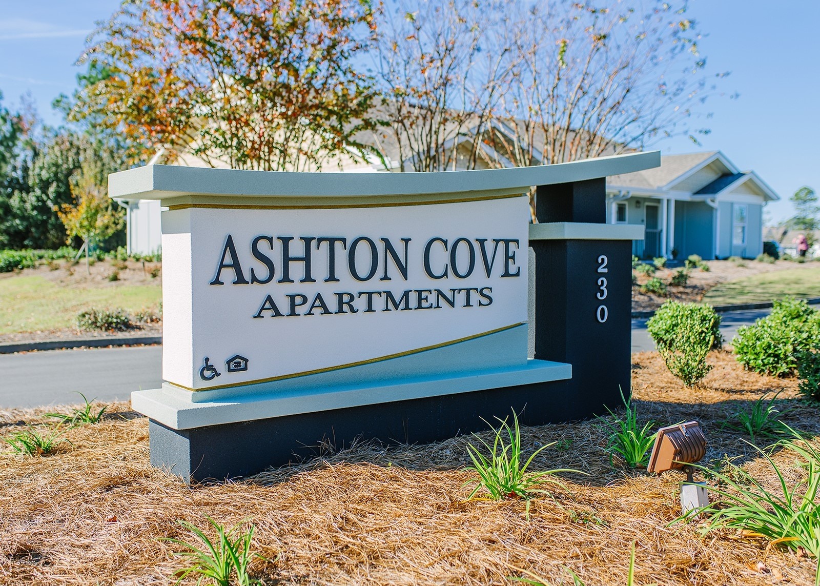 A sign for Ashton Cove Apartments is displayed in front of a grassy area.