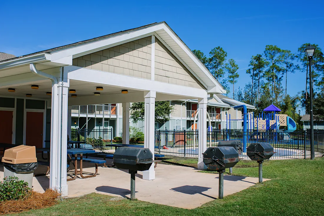 A white building with a porch and a playground in the background.
