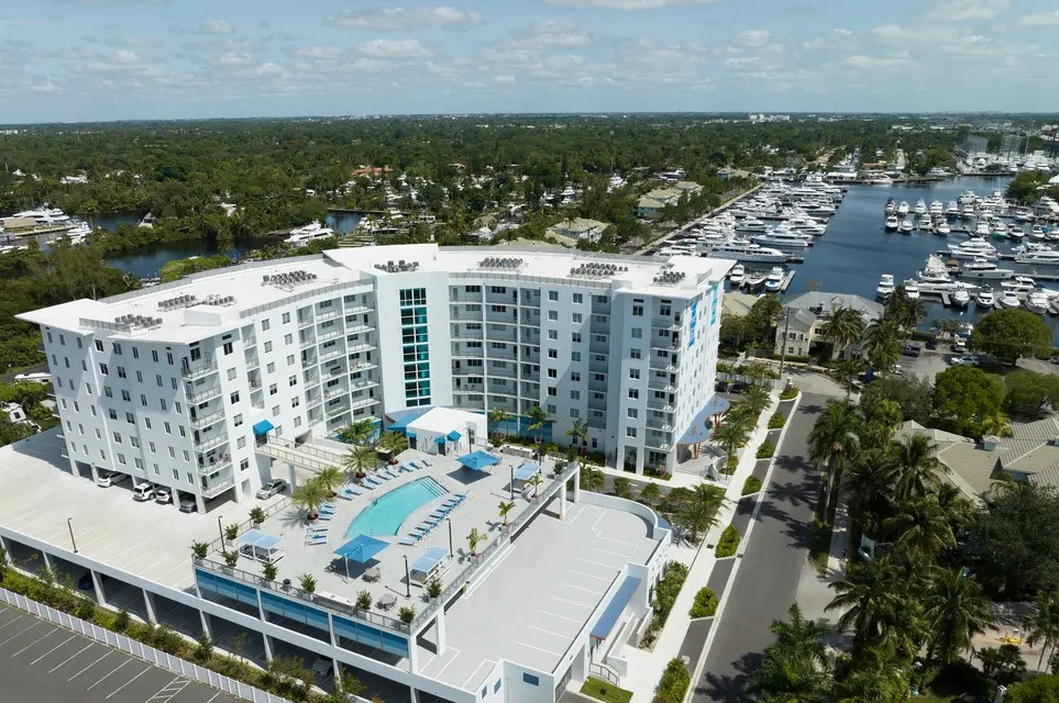 A large white hotel with a pool in the middle of a parking lot.