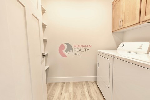 A white refrigerator is in a kitchen with a Rodman Realty Inc. logo on the wall.