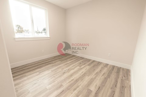 A room with wooden flooring and a window, branded with "PRODMAN REALTY INC."