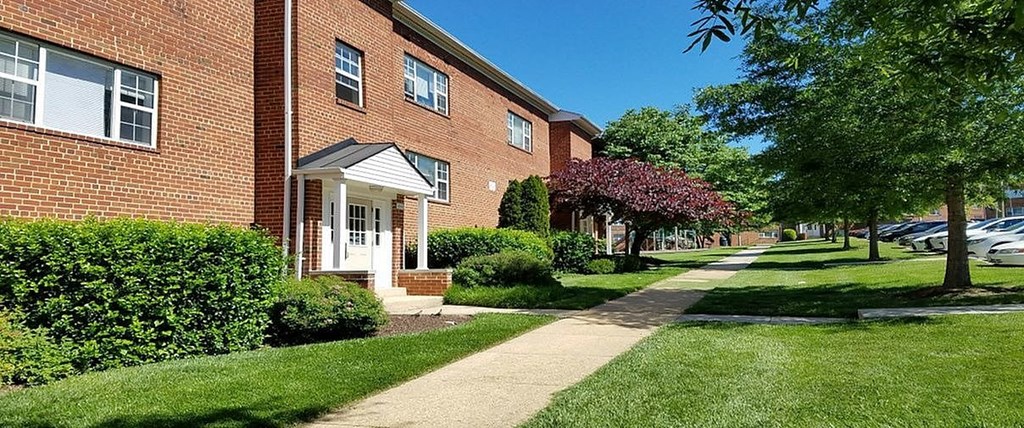 A brick building with a white door and windows is surrounded by greenery.