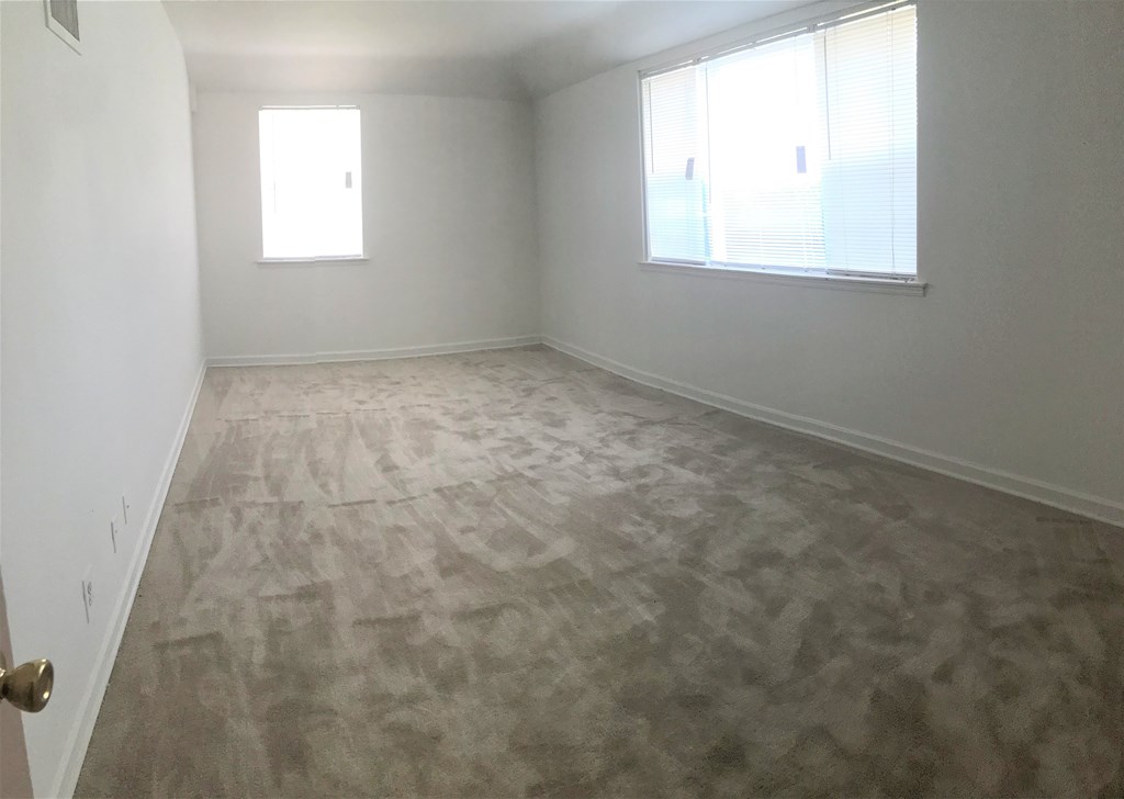 A room with a carpeted floor and two windows.